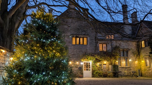 Grantham House at Christmas with golden lights strung along its façade and a huge Christmas tree with blue and gold lights to the left in the courtyard.